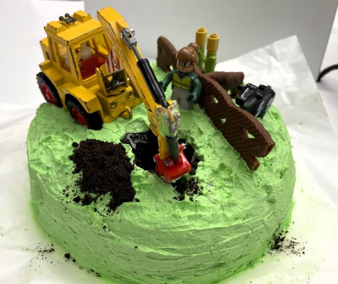 A cake that looks like a soil scientist describing a soil profile in a farm paddock using construction vehicle.