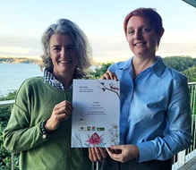 Two individuals hold a certificate with botanical illustrations