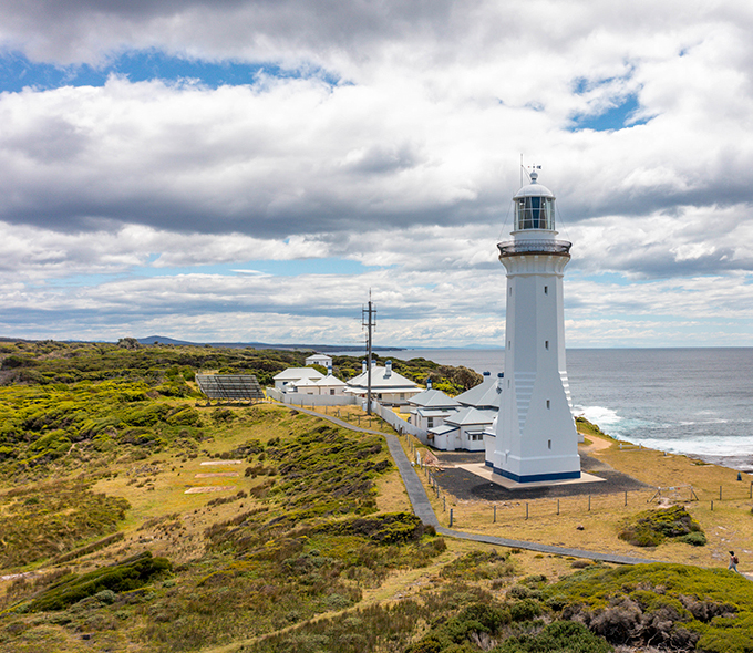 A white lighthouse overlooking the sea with surrounding greenery under a cloudy sky