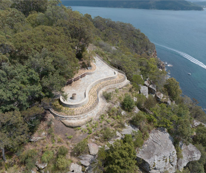 Aerial view of a wide curved stone lookout on a thickly forested rocky outcrop over the sea