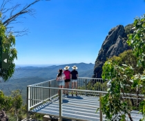 Three people in sunhats standing on West Kaputar Rock Lookout platform admiring the view and the blue sky in the distance