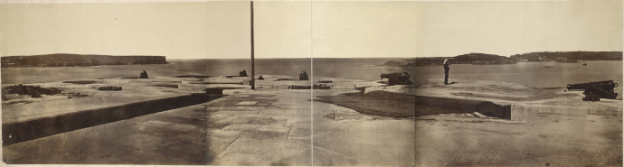 A sepia-toned archival photograph showing cannons and fortifications looking over the harbour, with other headlands visible in the distance