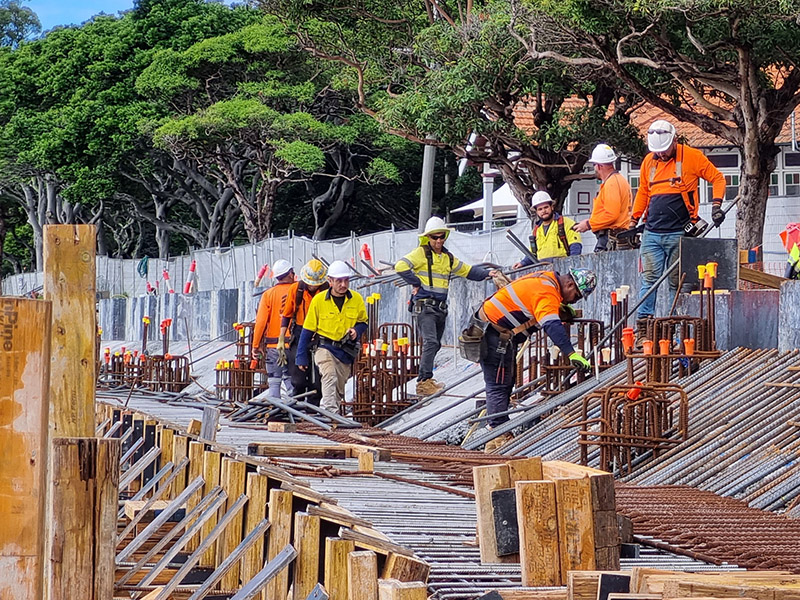 Construction workers in safety gear assembling reinforcement bars at a construction site with wooden formwork and orange safety markers