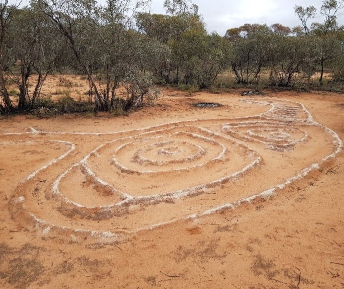 Aboriginal rock patterns created in red sand, with scrubby trees in the background