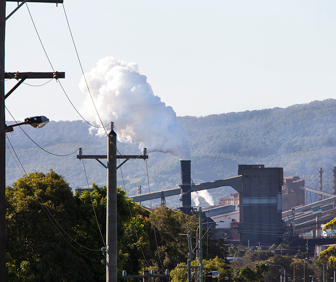 View of Bluescope Steel steelworks from surrounding streets, Port Kembla, with escarpment in the background and steam/pollution rising from one of the stacks