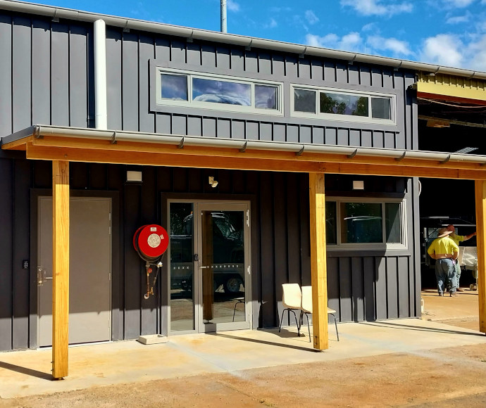 A squat grey building with a timber veranda in full sunlight under a bright blue sky