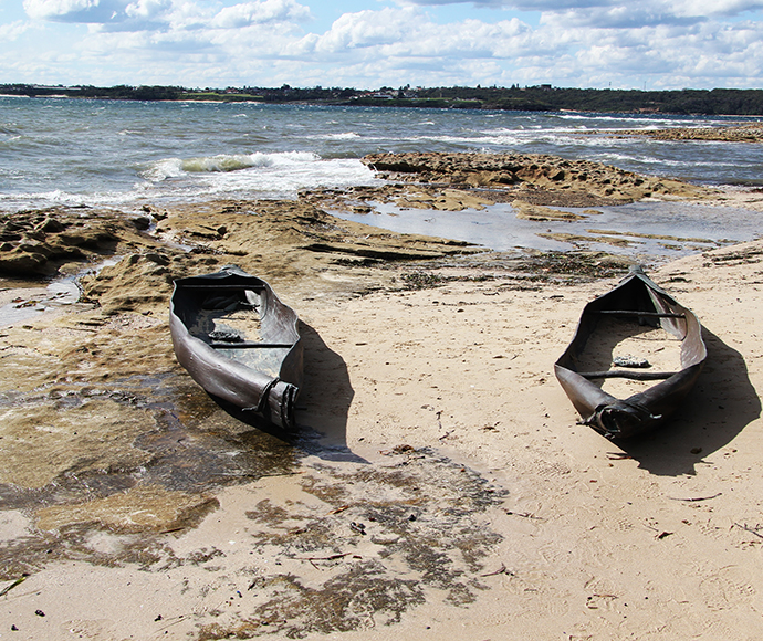 Nuwi Canoe Sculptures - Shore View: Two "Nuwi" canoe sculptures set against a sandy shore, symbolizing Aboriginal heritage and seafaring traditions at Kamay Botany Bay National Park.