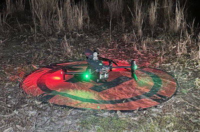 A drone set up to do a night flight to monitor koalas. The drone is on a round material pad on the ground and has its red and green lights on 