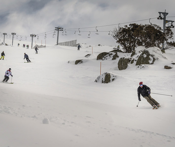 Downhill skiers at Perisher with T-bar, rocks and snow-gums in the background