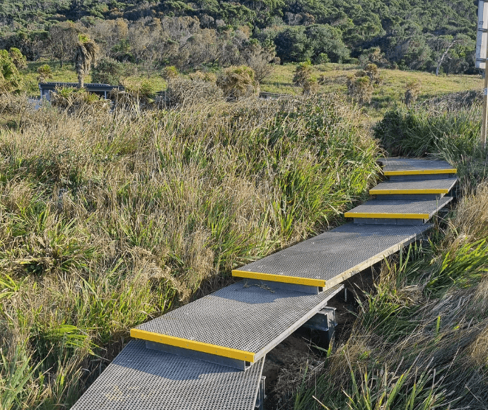 Gray ascending steps with yellow strips surrounded by green bushland.