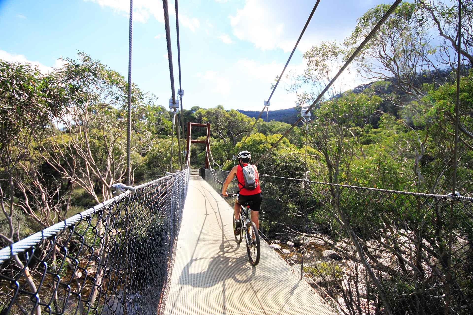 Man in red top and helmet cycling across bridge