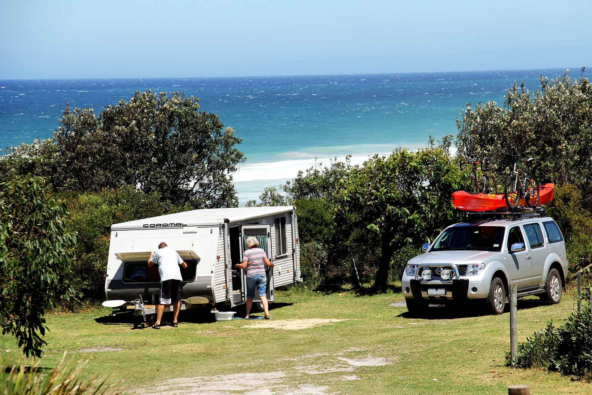 Two people unpacking a capervan, vehicle nearby, beach in background