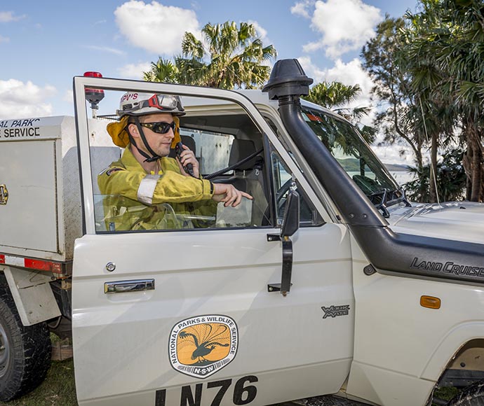 NPWS officr standing with the door of his vehicle open while he talks on the radio. 