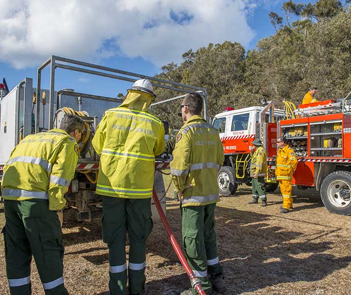 5 volunteer fire fighters standing between 2 fire trucks, inspecting a hose.