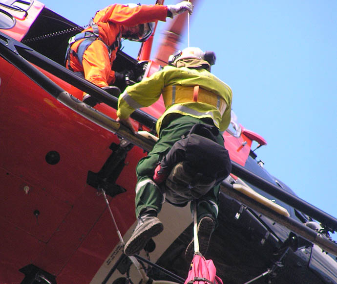 Person in high-visibility gear being lowered out of a helicopter